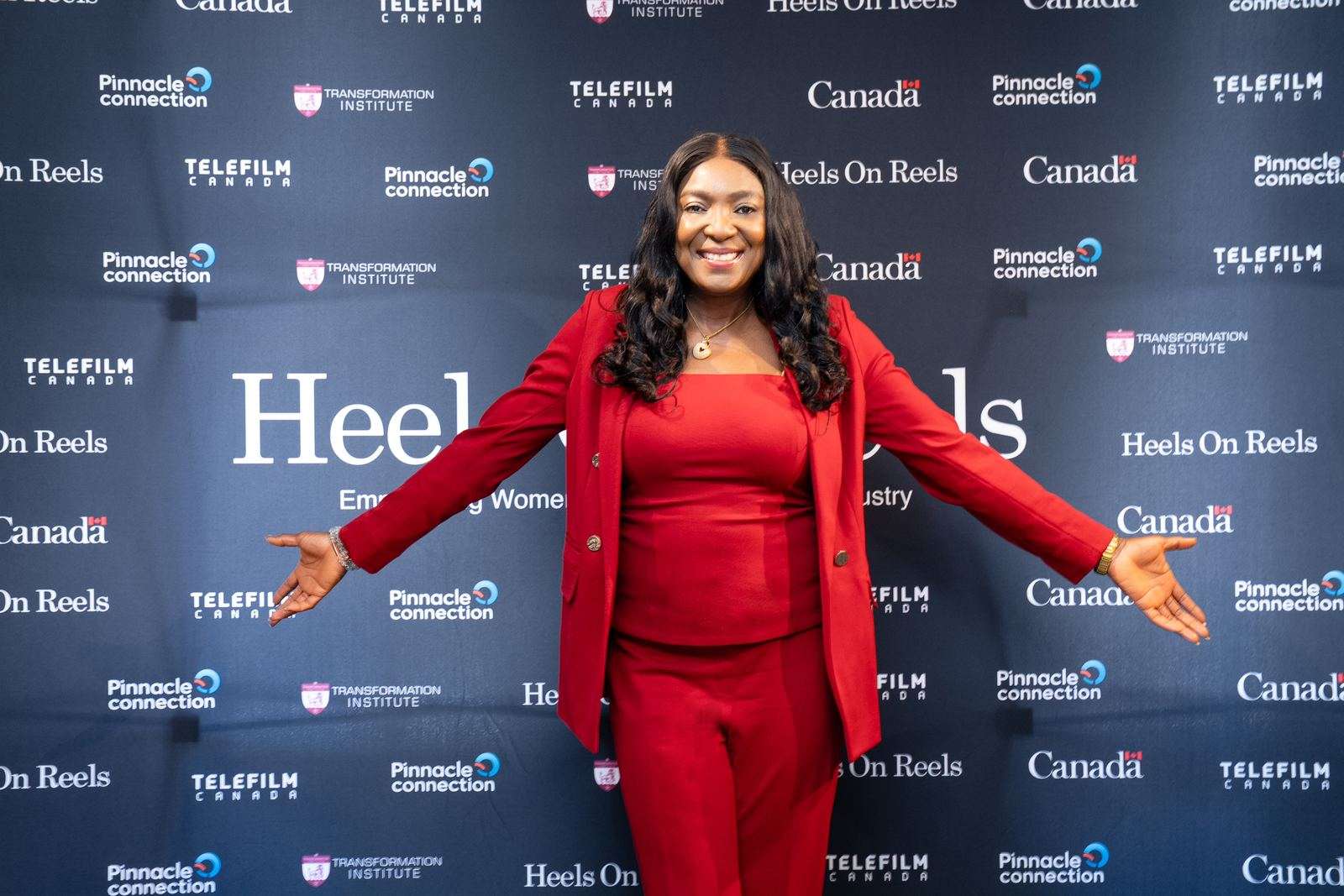 A director standing arms open in front of the Heels On Reels media backdrop